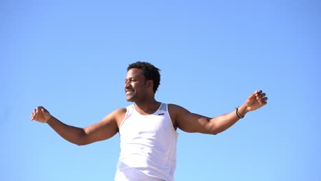 Smiling-young-man-exercising-against-blue-sky